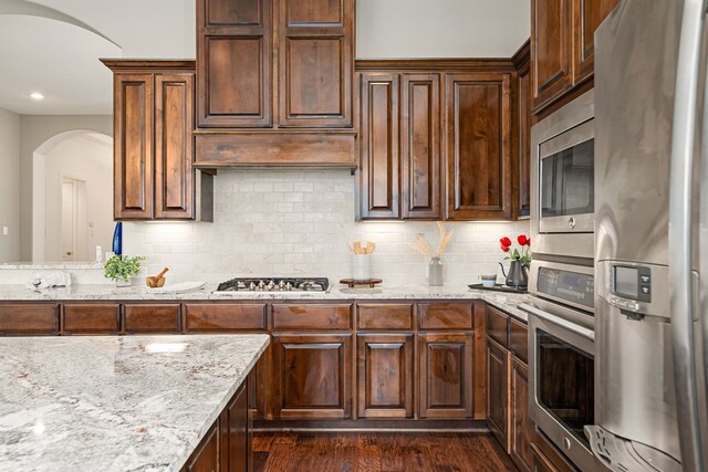 kitchen with appliances with stainless steel finishes, arched walkways, light stone countertops, tasteful backsplash, and recessed lighting