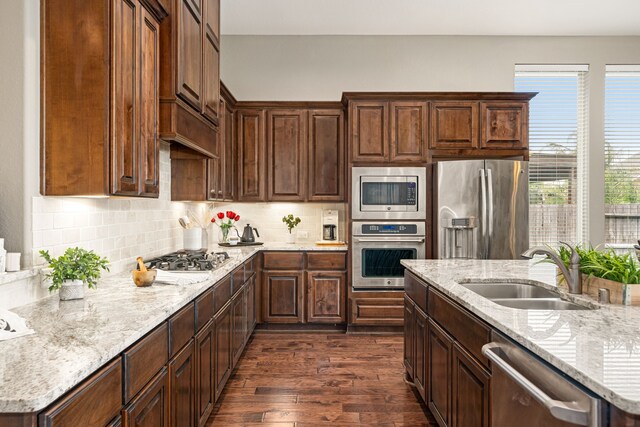 kitchen featuring appliances with stainless steel finishes, a sink, dark wood finished floors, tasteful backsplash, and light stone countertops