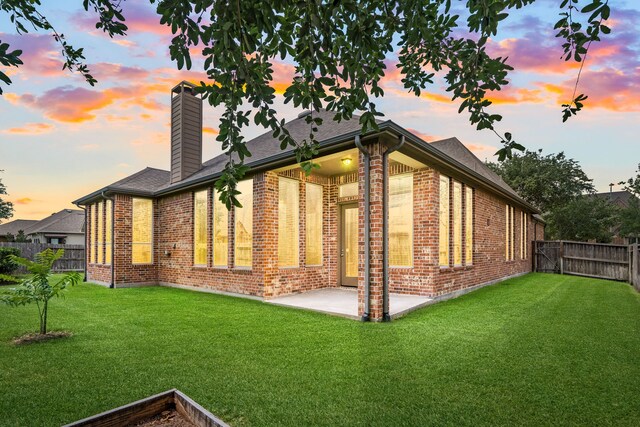back of property with brick siding, a chimney, a patio area, and roof with shingles