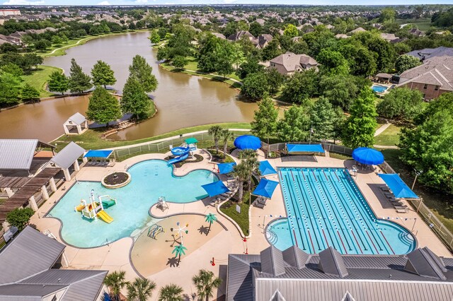 drone / aerial view of a pool, a nearby body of water, and a tree filled landscape
