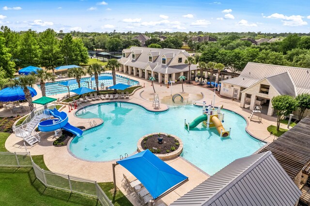 community pool with a water slide, fence, a water play area, a patio, and view of scattered trees