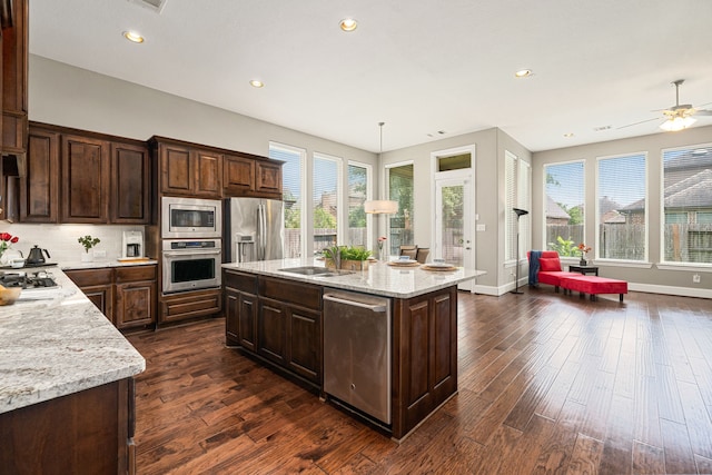 kitchen with stainless steel appliances, dark wood finished floors, an island with sink, recessed lighting, and light stone counters