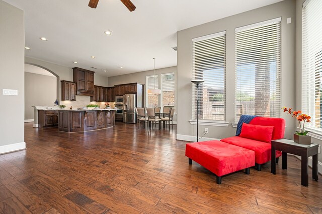 living room featuring baseboards, arched walkways, dark wood-type flooring, healthy amount of natural light, and recessed lighting