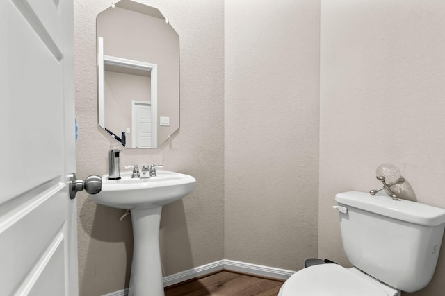 half bathroom featuring toilet, wood finished floors, and baseboards