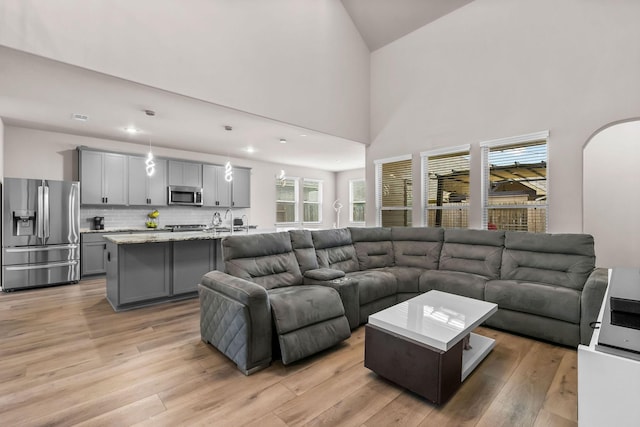 living room with light wood-style flooring, arched walkways, and high vaulted ceiling