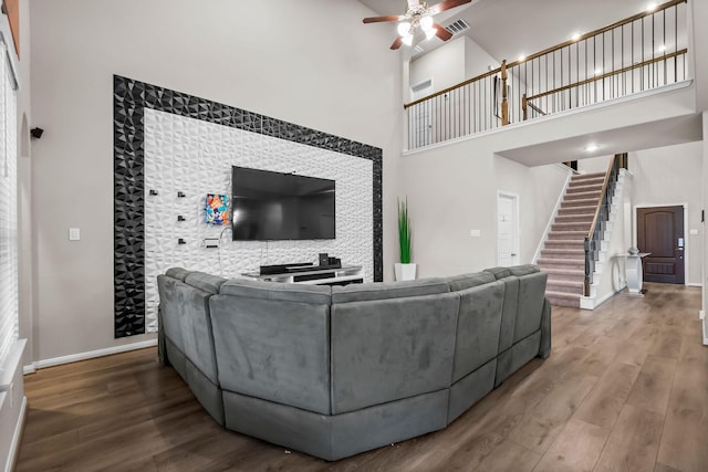 living room with stairs, wood finished floors, a towering ceiling, a ceiling fan, and baseboards