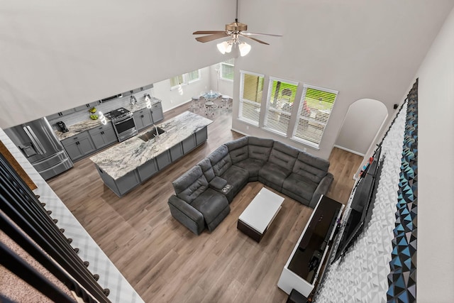 living room featuring light wood finished floors, a towering ceiling, and a ceiling fan
