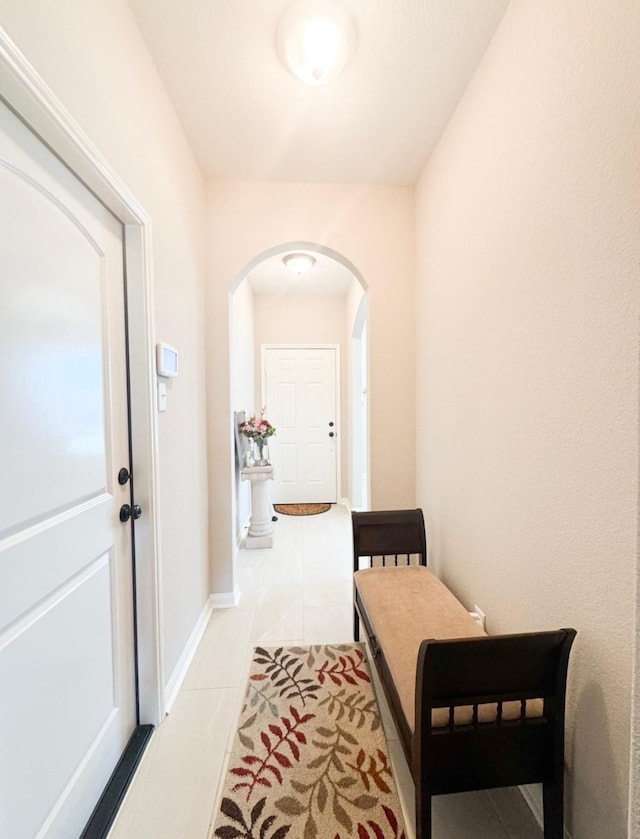 hallway with arched walkways, tile patterned flooring, and baseboards