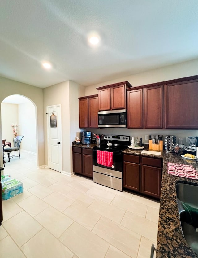 kitchen featuring stainless steel appliances, arched walkways, a sink, light tile patterned floors, and recessed lighting