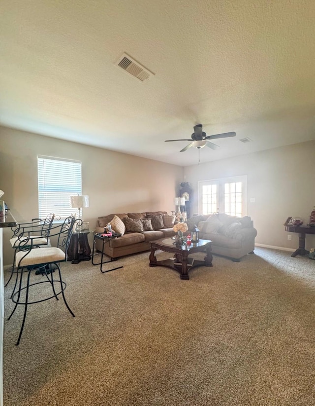 carpeted living room with ceiling fan, baseboards, and a textured ceiling