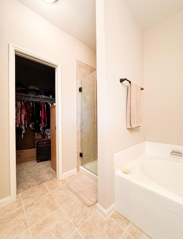 full bath featuring a shower stall, a walk in closet, a garden tub, and tile patterned flooring