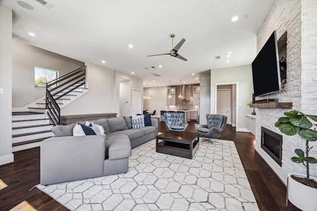 living area featuring a fireplace, dark wood-style flooring, stairs, and a ceiling fan