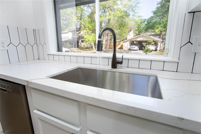details featuring light stone countertops, stainless steel dishwasher, tasteful backsplash, a sink, and white cabinets