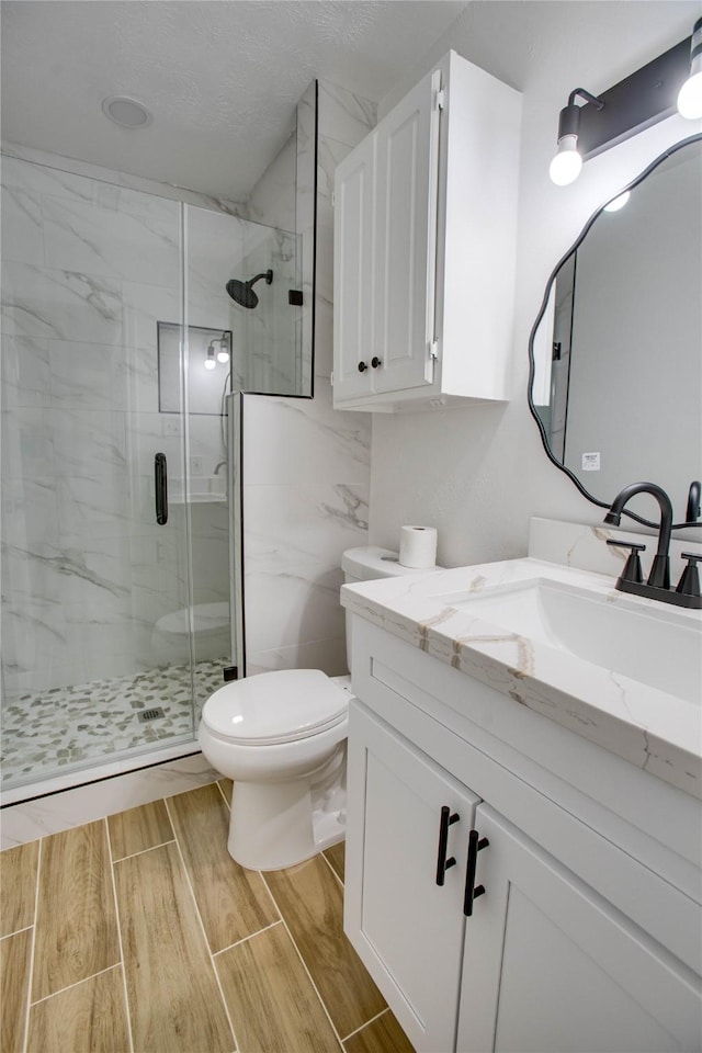 full bath featuring toilet, a marble finish shower, vanity, and wood finish floors