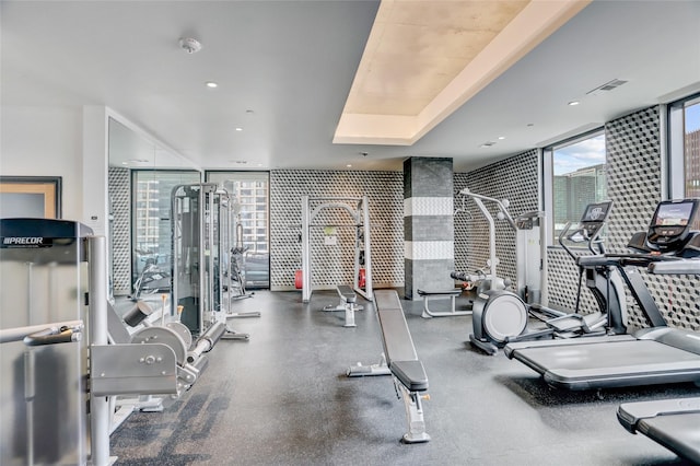 gym featuring a tray ceiling, recessed lighting, and floor to ceiling windows