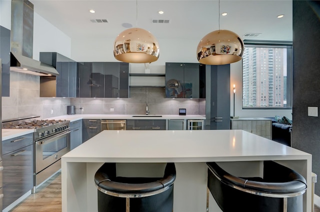 kitchen with a sink, gray cabinets, modern cabinets, wall chimney range hood, and appliances with stainless steel finishes