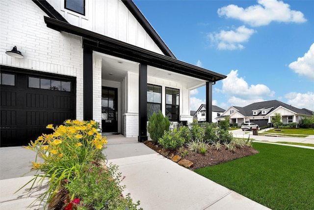 view of exterior entry featuring a porch, brick siding, a residential view, a yard, and board and batten siding