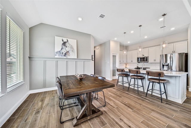 dining room featuring light wood finished floors, visible vents, lofted ceiling, and wainscoting