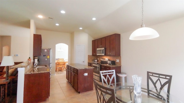 15407 Vincennes Oak St, Cypress, TX 77429 - kitchen featuring light tile patterned floors, arched walkways, appliances with stainless steel finishes, a kitchen island, and light stone counters