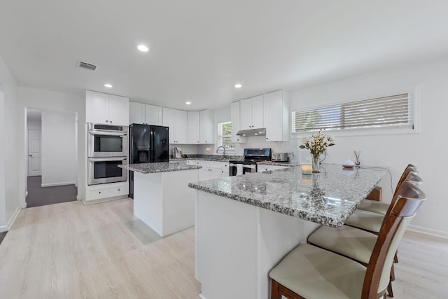 kitchen featuring a peninsula, visible vents, under cabinet range hood, light stone countertops, and appliances with stainless steel finishes