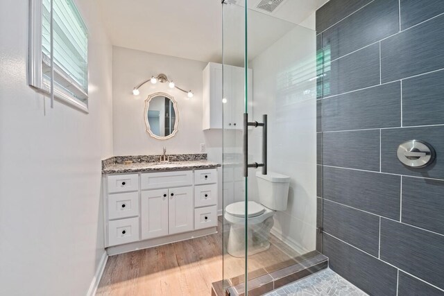 bathroom featuring toilet, wood finished floors, vanity, visible vents, and tiled shower