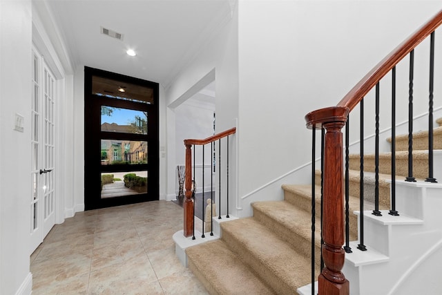 foyer entrance featuring crown molding, visible vents, tile patterned flooring, baseboards, and stairs