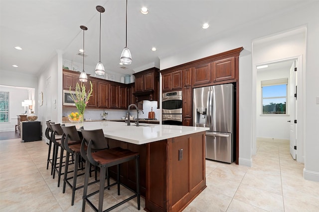 kitchen with a sink, stainless steel appliances, a large island with sink, light countertops, and hanging light fixtures