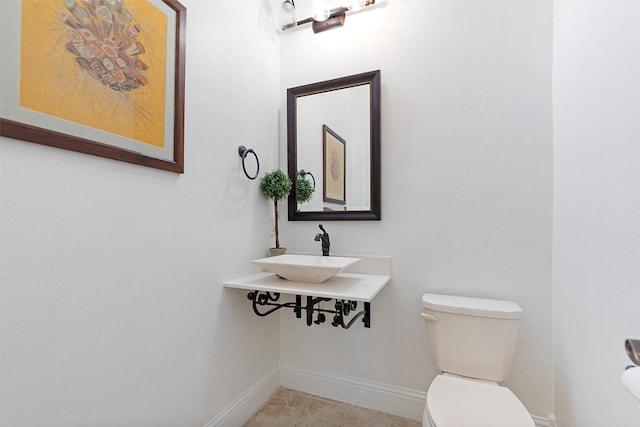 half bath with baseboards, tile patterned flooring, toilet, and a sink