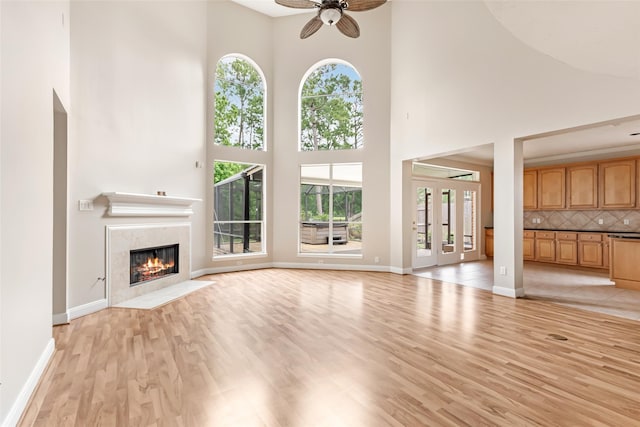 unfurnished living room with a ceiling fan, a wealth of natural light, a high end fireplace, and a high ceiling