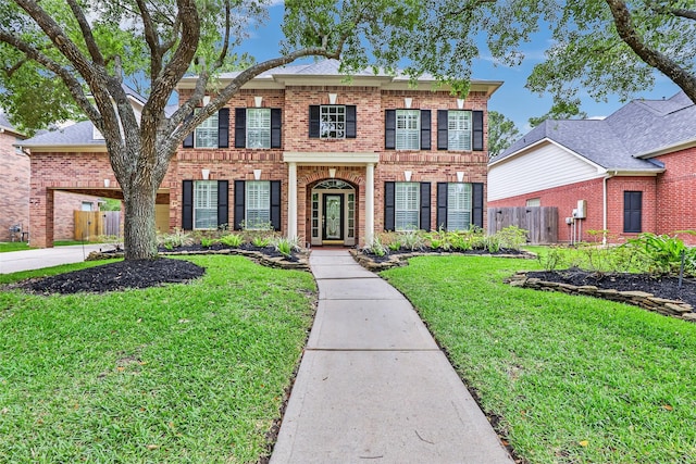 colonial inspired home with brick siding, fence, and a front yard