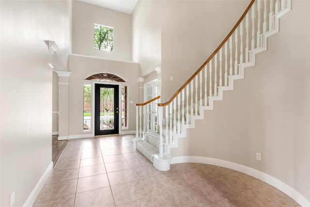 tiled foyer entrance with stairway, baseboards, and a towering ceiling