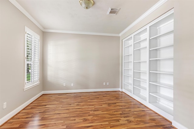 unfurnished room featuring wood finished floors, visible vents, baseboards, and built in shelves
