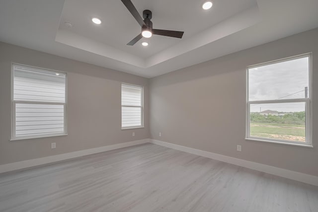 unfurnished room with recessed lighting, ceiling fan, a tray ceiling, baseboards, and light wood-style floors