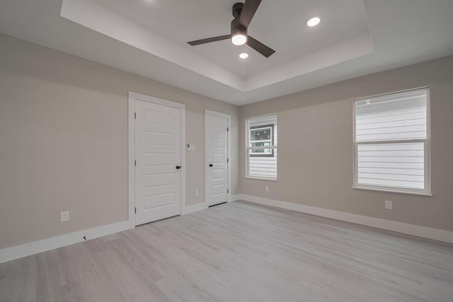 unfurnished bedroom with baseboards, a raised ceiling, light wood-style floors, and recessed lighting