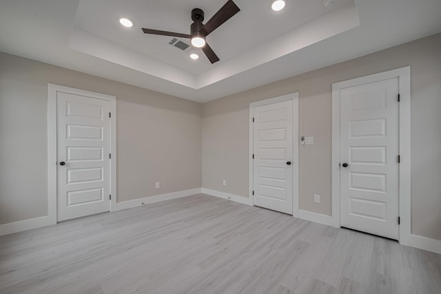 unfurnished bedroom featuring a tray ceiling, visible vents, light wood-style flooring, and baseboards