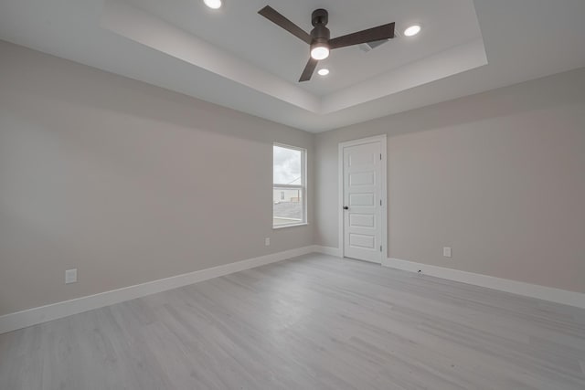 empty room featuring a ceiling fan, a raised ceiling, baseboards, and light wood finished floors