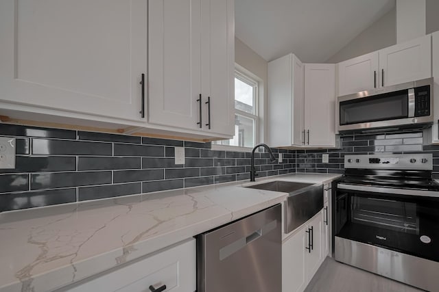 kitchen with lofted ceiling, stainless steel appliances, white cabinetry, decorative backsplash, and light stone countertops