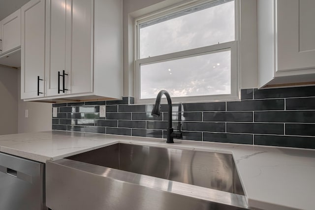 kitchen with a sink, light stone counters, dishwasher, white cabinetry, and backsplash