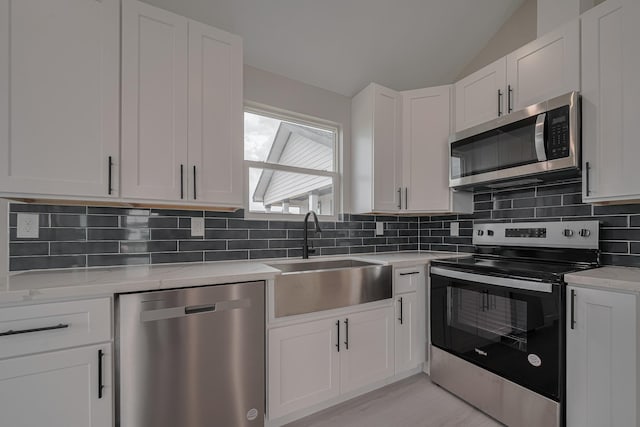 kitchen with lofted ceiling, a sink, decorative backsplash, stainless steel appliances, and white cabinets