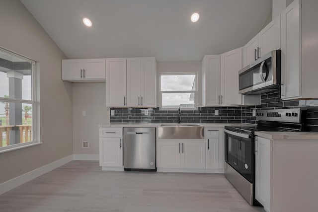 kitchen with a sink, white cabinetry, appliances with stainless steel finishes, vaulted ceiling, and tasteful backsplash