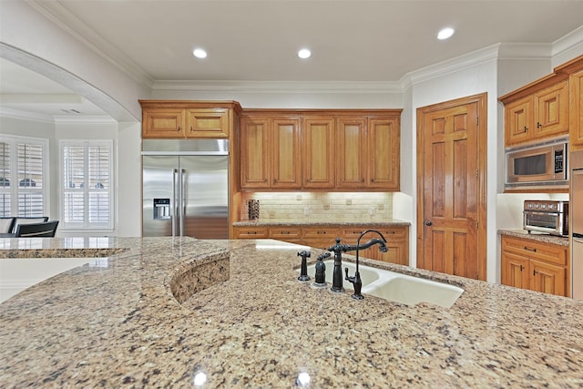 kitchen with built in appliances, light stone countertops, arched walkways, a sink, and backsplash