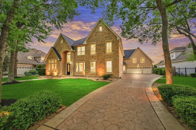 traditional-style home with a yard, fence, decorative driveway, an attached garage, and stone siding