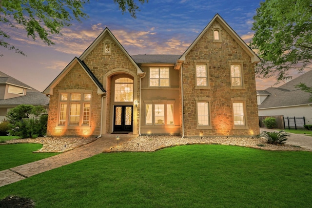 view of front of home featuring a lawn, stone siding, french doors, and fence