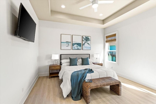 bedroom with recessed lighting, light wood finished floors, a ceiling fan, a raised ceiling, and baseboards