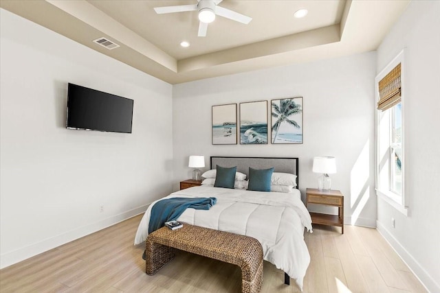 bedroom featuring a tray ceiling, light wood-style floors, visible vents, and baseboards