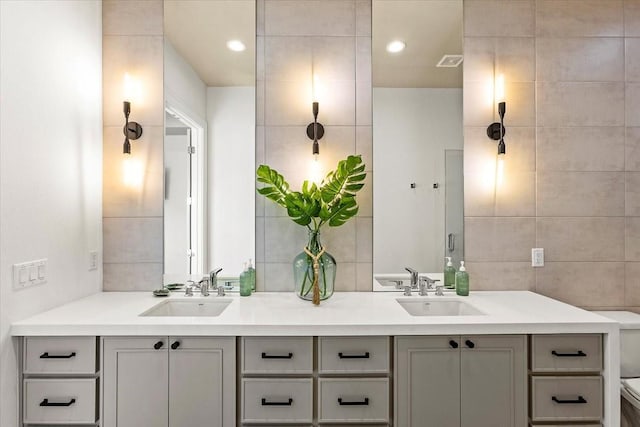 bathroom with tile walls, toilet, visible vents, and a sink