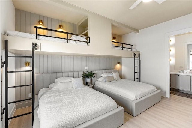 bedroom with ensuite bath, light wood-style flooring, wood walls, and a sink