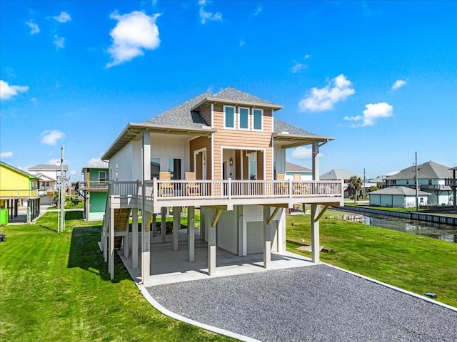 rear view of property featuring a lawn, an attached garage, gravel driveway, a shingled roof, and a carport