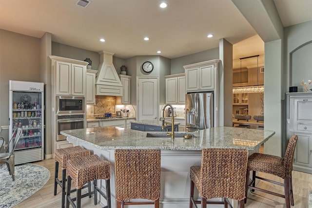 18787 Serene Water Dr, Montgomery, TX 77356 - kitchen featuring a sink, a large island with sink, custom exhaust hood, decorative backsplash, and appliances with stainless steel finishes