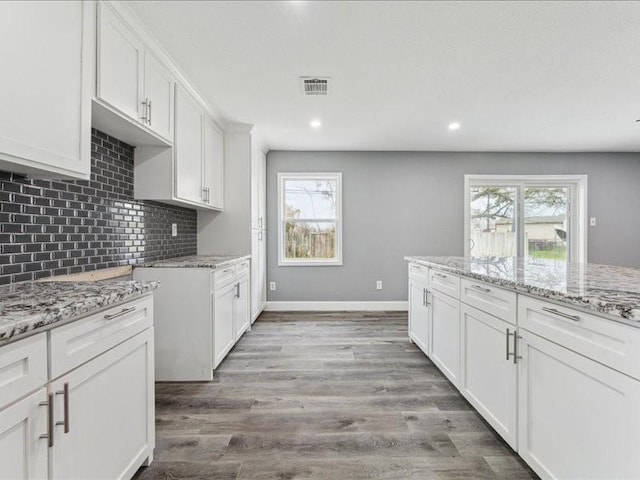 kitchen with backsplash, a wealth of natural light, light stone countertops, and visible vents